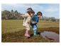 Deux enfants en vêtements de pluie et en bottes jouent dans une flaque de boue.