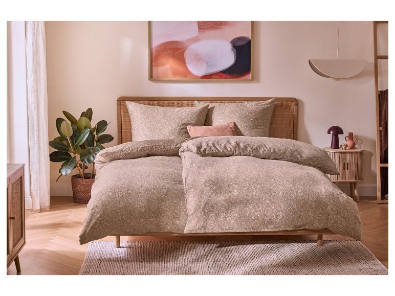 Chambre avec lit en bois, parure de lit beige à motifs et plante.