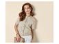 Femme en cardigan beige à manches courtes et pantalon blanc, tenant une pochette.