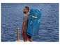 Un homme porte un paddleboard gonflable Hydro-Force sur le dos.