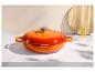 Cocotte en fonte orange sur une surface en marbre blanc avec une planche en bois et une bouteille d'huile.