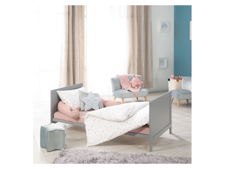 Un lit d'enfant gris avec des draps roses et des oreillers étoilés.