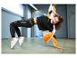 Femme en leggings de sport noirs et veste orange-noir-blanc s'étire.