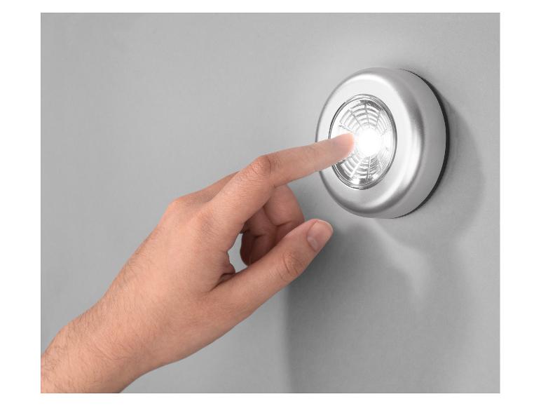 Main appuyant sur une lumière LED ronde argentée sur un mur gris