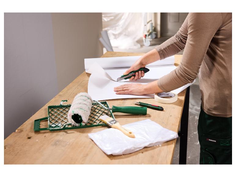 Une personne coupe du papier peint avec un cutter, avec des outils de peinture sur la table.