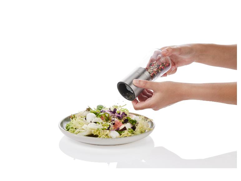 Une main tient un moulin à poivre au-dessus d'une salade avec de la mozzarella et des figues.