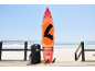 Paddleboard orange avec accessoires et sac sur une promenade en bois au bord de la plage.