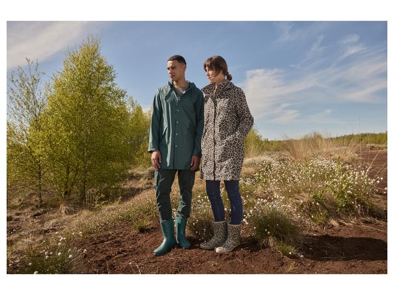 Un couple en imperméables et bottes de pluie devant des arbres verts et un ciel bleu.
