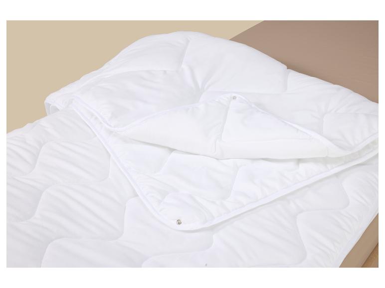 Couette blanche matelassée avec boutons-pression sur un lit marron clair.