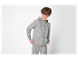 Un garçon sourit en portant un sweat à capuche gris et un pantalon de jogging.