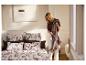 Une femme tient un plaid marron LIVARNO® à franges à côté du lit.