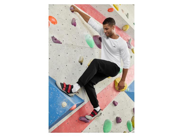 Homme en haut blanc à manches longues et pantalon de jogging noir faisant de l'escalade en salle.