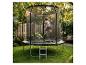 Fille sautant sur un trampoline avec filet de sécurité dans un jardin vert.
