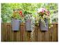 Pots de fleurs en plastique gris avec des fleurs colorées suspendus à une clôture en bois.