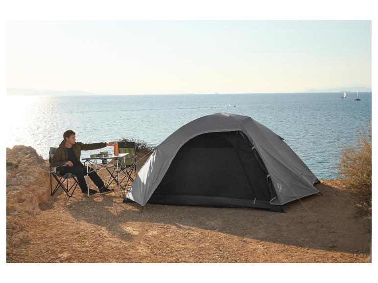 Homme campant au bord de la mer avec une tente CRIVIT, des chaises pliantes et une table.