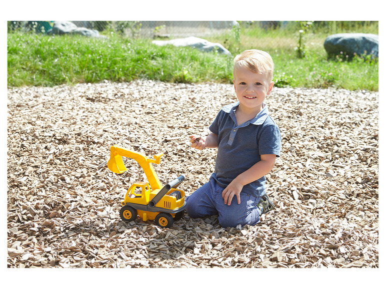 Un enfant joue avec une grue jaune en plastique dans une aire de jeux.