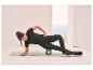 Femme en tenue de sport noire utilisant un rouleau de massage sur un tapis de yoga.