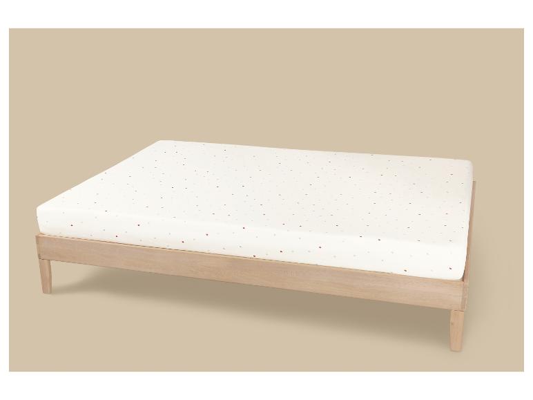 Lit en bois avec matelas blanc à pois colorés sur fond beige.