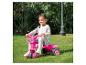 Une petite fille roule en tricycle rose Barbie dans le jardin.