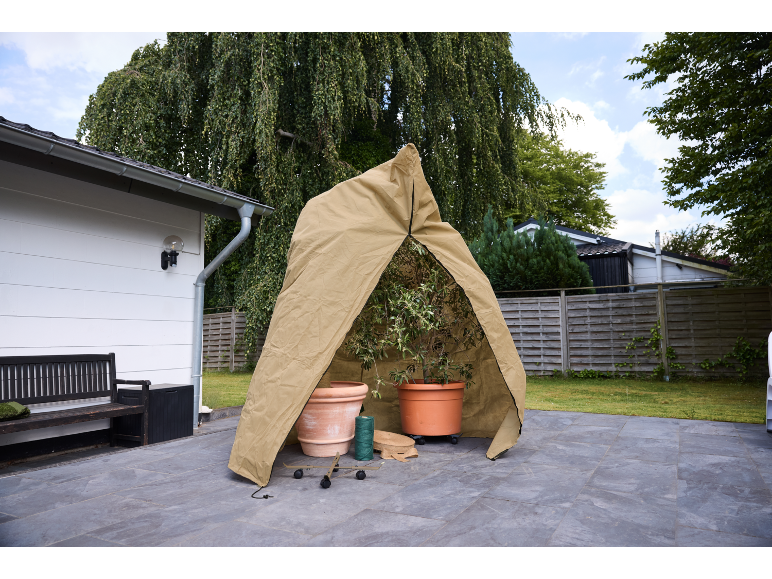 Housse de protection pour plantes avec fermeture éclair, abritant deux plantes en pot sur une terrasse.
