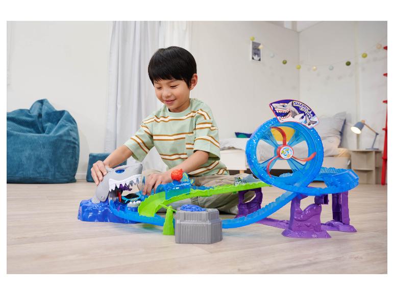Un garçon joue avec un circuit Hot Wheels Shark Cyclone sur le sol.