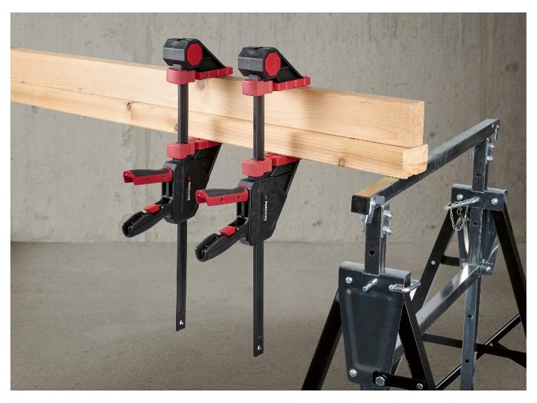 Deux serre-joints fixant des planches de bois sur un tréteau métallique.