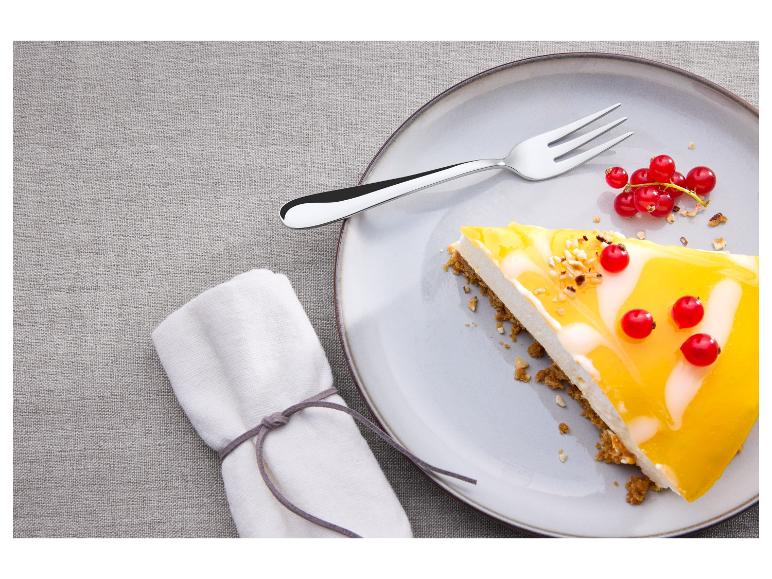 Une part de cheesecake avec un nappage à la mangue et des groseilles rouges sur une assiette avec une fourchette.