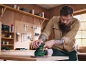Homme barbu utilisant une ponceuse électrique dans un atelier de menuiserie.