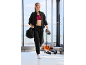 Une femme en survêtement noir et brassière de sport rouge marche dans une salle de sport.