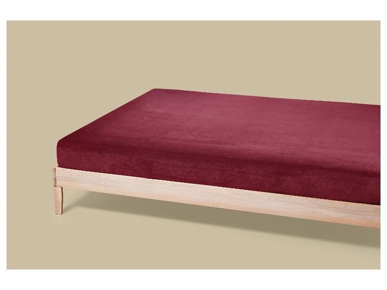 Drap-housse en velours bordeaux sur un cadre de lit en bois clair.