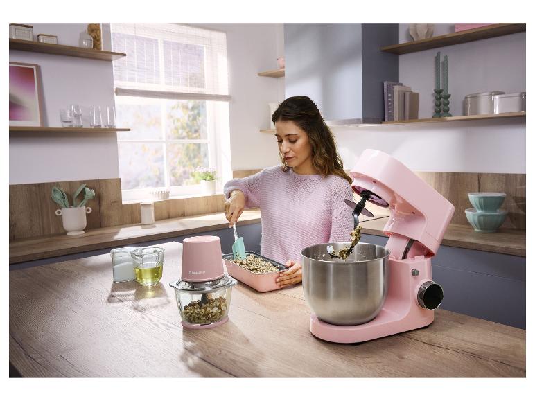 Femme cuisine dans une cuisine avec un robot pâtissier et un hachoir roses.