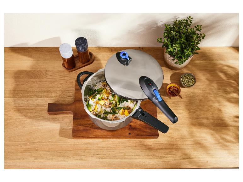 Une cocotte-minute avec du riz et des légumes, des épices et une plante sur une table en bois.