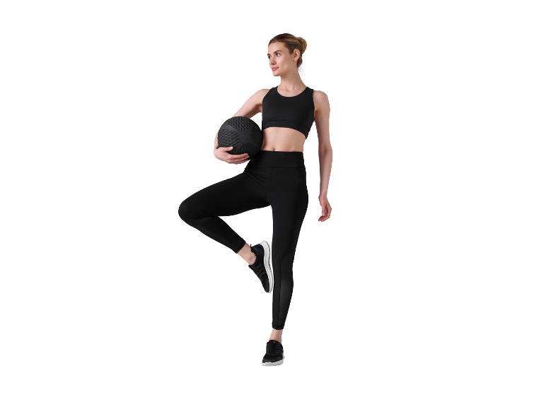 Femme en tenue de sport noire tenant un ballon lesté, en équilibre sur une jambe.