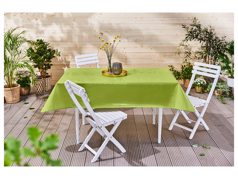 Une nappe verte sur une table en bois avec des chaises pliantes blanches.