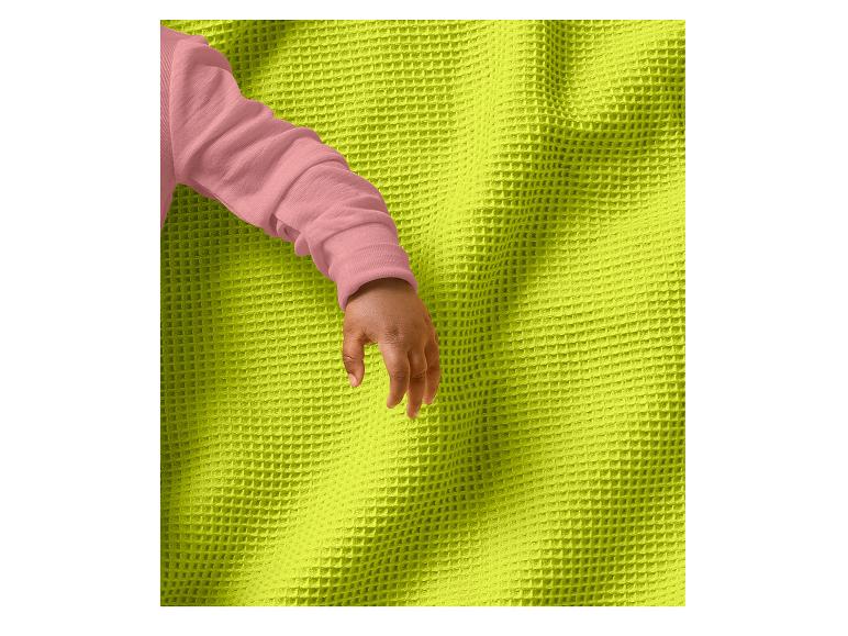 Main de bébé avec manche rose sur une couverture gaufrée vert lime