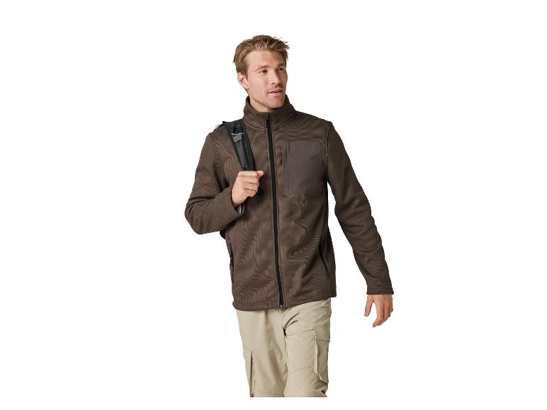 Homme en veste polaire marron et pantalon beige avec un sac à dos sur l'épaule.