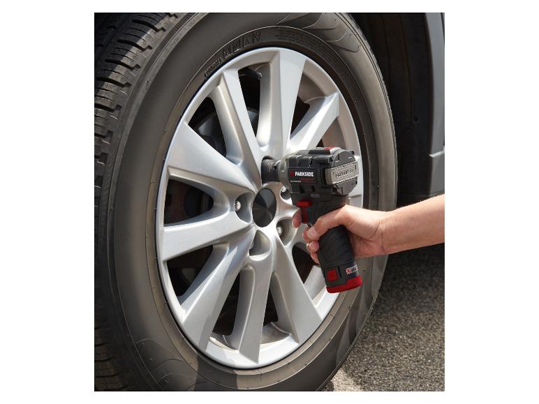 Main tenant une clé à chocs sans fil sur une roue de voiture.