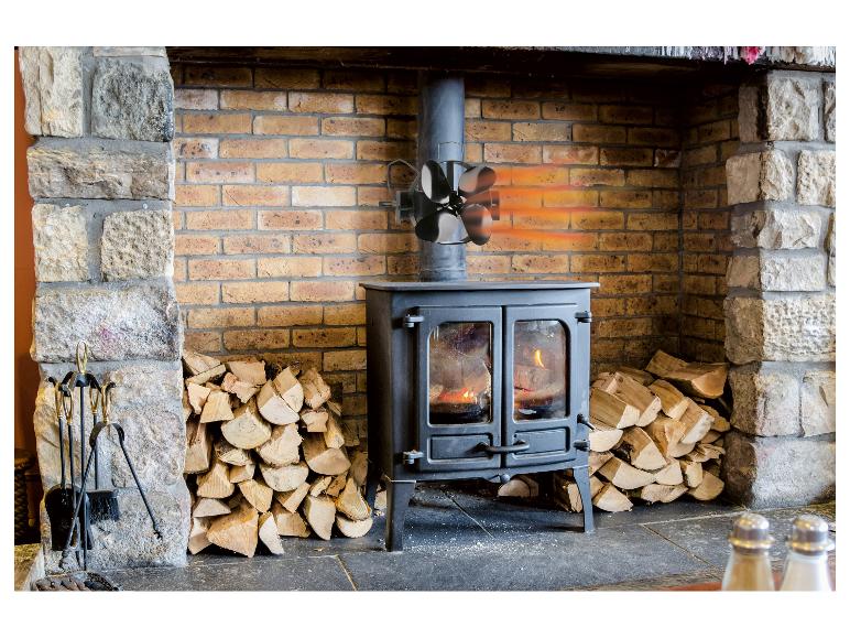Poêle à bois avec ventilateur de distribution de chaleur et piles de bois dans une cheminée en pierre et brique.
