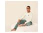 Homme assis sur un pouf beige, portant un t-shirt crème à manches longues et un pantalon en velours vert.