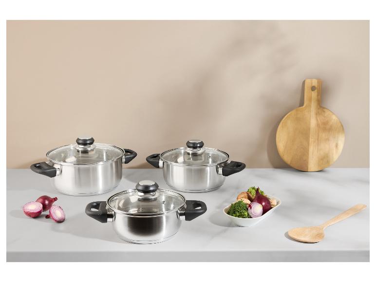 Trois casseroles en acier inoxydable avec couvercles en verre, oignons rouges, légumes et une planche à découper en bois.