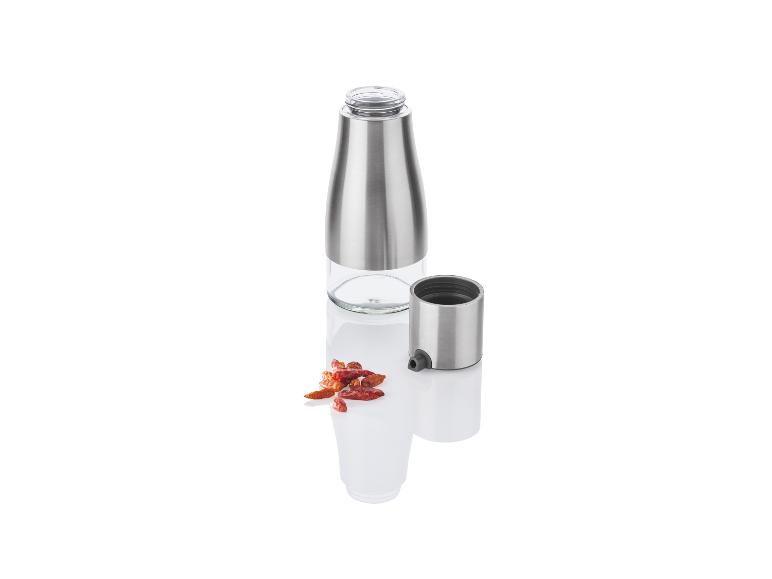 Une bouteille en acier inoxydable avec un embout pulvérisateur pour l'huile et le vinaigre, à côté de piments séchés.