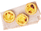 Trois tartelettes portugaises à la crème sur une serviette rose clair, vue de dessus.