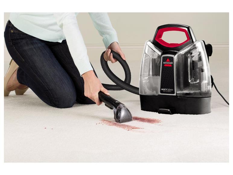 Personne nettoyant une tache rouge sur un tapis blanc avec un nettoyeur de taches Bissell Multiclean.