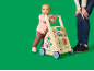 Bébé jouant avec un trotteur d'activités en bois, avec un adulte à côté.