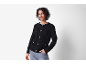 Femme souriante en cardigan noir texturé et jean, main dans la poche.