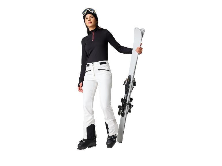Femme en tenue de ski noire et blanche, tenant des skis.
