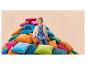 Fille en robe bleue et cardigan assise sur une pile de coussins colorés.