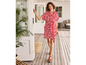 Une femme portant une robe rouge à imprimé blanc marche sur une terrasse en bois.