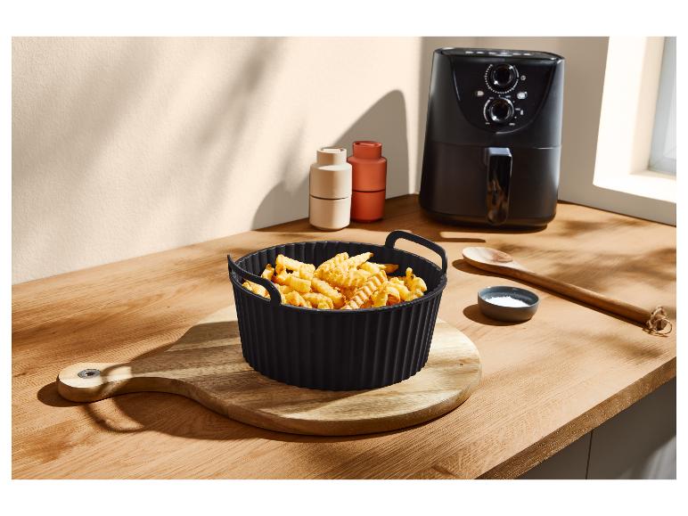 Friteuse à air avec un panier de frites ondulées, une cuillère en bois et du sel sur une table en bois.