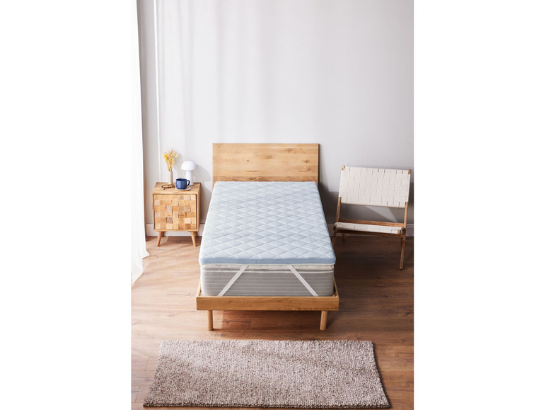 Un surmatelas bleu clair sur un cadre de lit en bois avec un tapis.